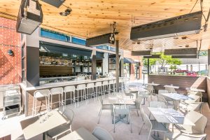 Restaurant outdoor patio that has a bar with light colored stools and tables and chairs