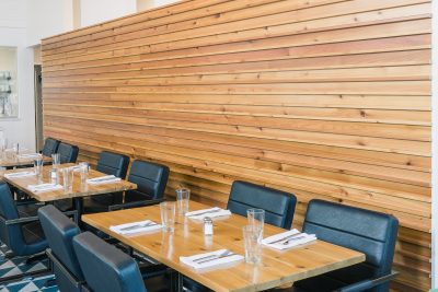 Wood accent wall behind restaurant seating with black chairs and wood top tables