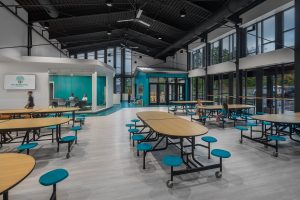 Photo-Cafeteria with lunch room tables, exposed ceilings and main entrance views