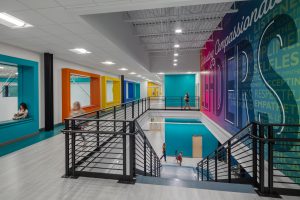 Photo-Corridor with view of brightly colored windows over looking the gym and stairwell to lower level