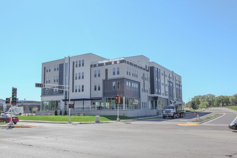 exterior of cream, white and gray four story retail and apartments from across the street