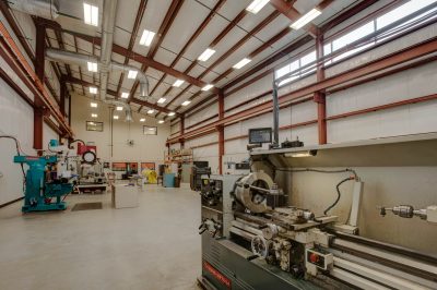 industrial workshop with high ceilings and large windows. Metal shelves line the walls filled with supplies.