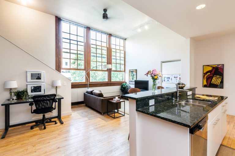 Open concept living room and kitchen with expansive windows, wood flooring and dark colored granite countertops