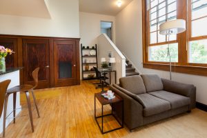 Apartment living room space with couch light colored floors and stairwell to upper level