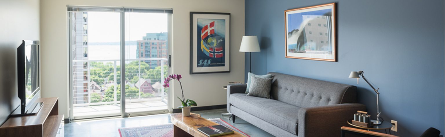 Apartment Living room with dark wood floors, dark blue accent wall behind the couch and sliding glass door to balcony