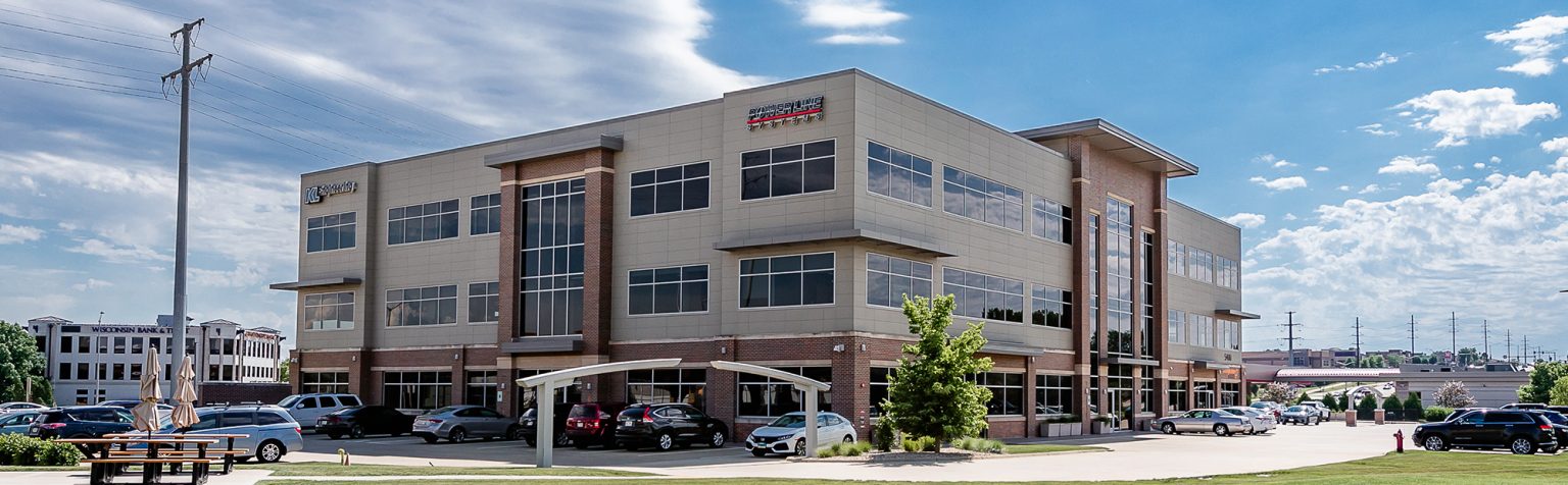 multi-story office building with large windows, brown colored bricks and light brown siding.