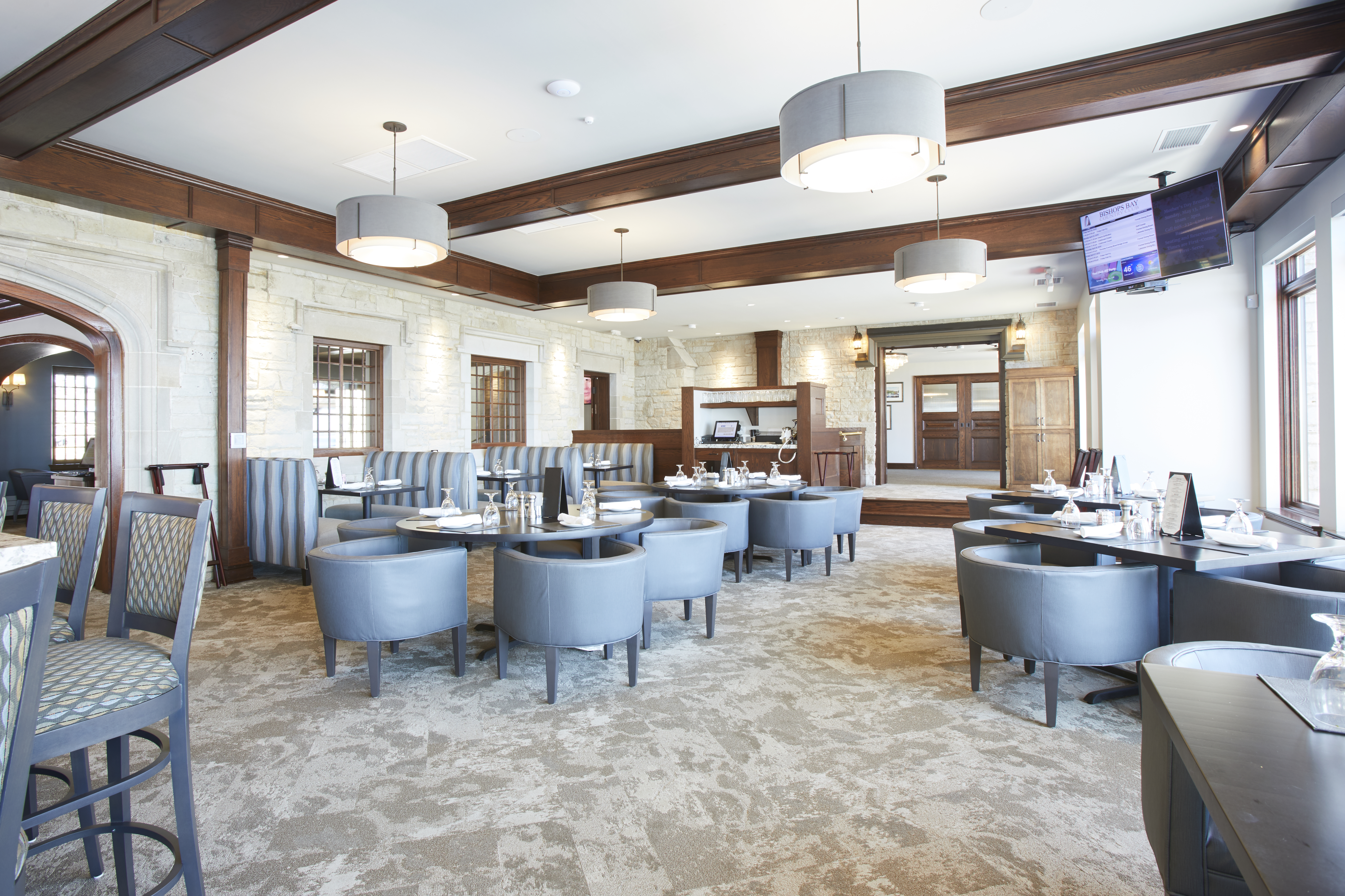 Wide view of restaurant seating area with wood accents, carpeted floor, and light gray chairs