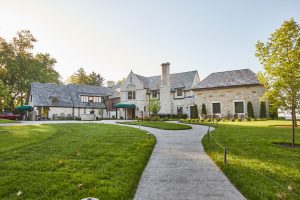 Exterior shot of cream colored bricks, grassy front lawn and concrete path up to the front door