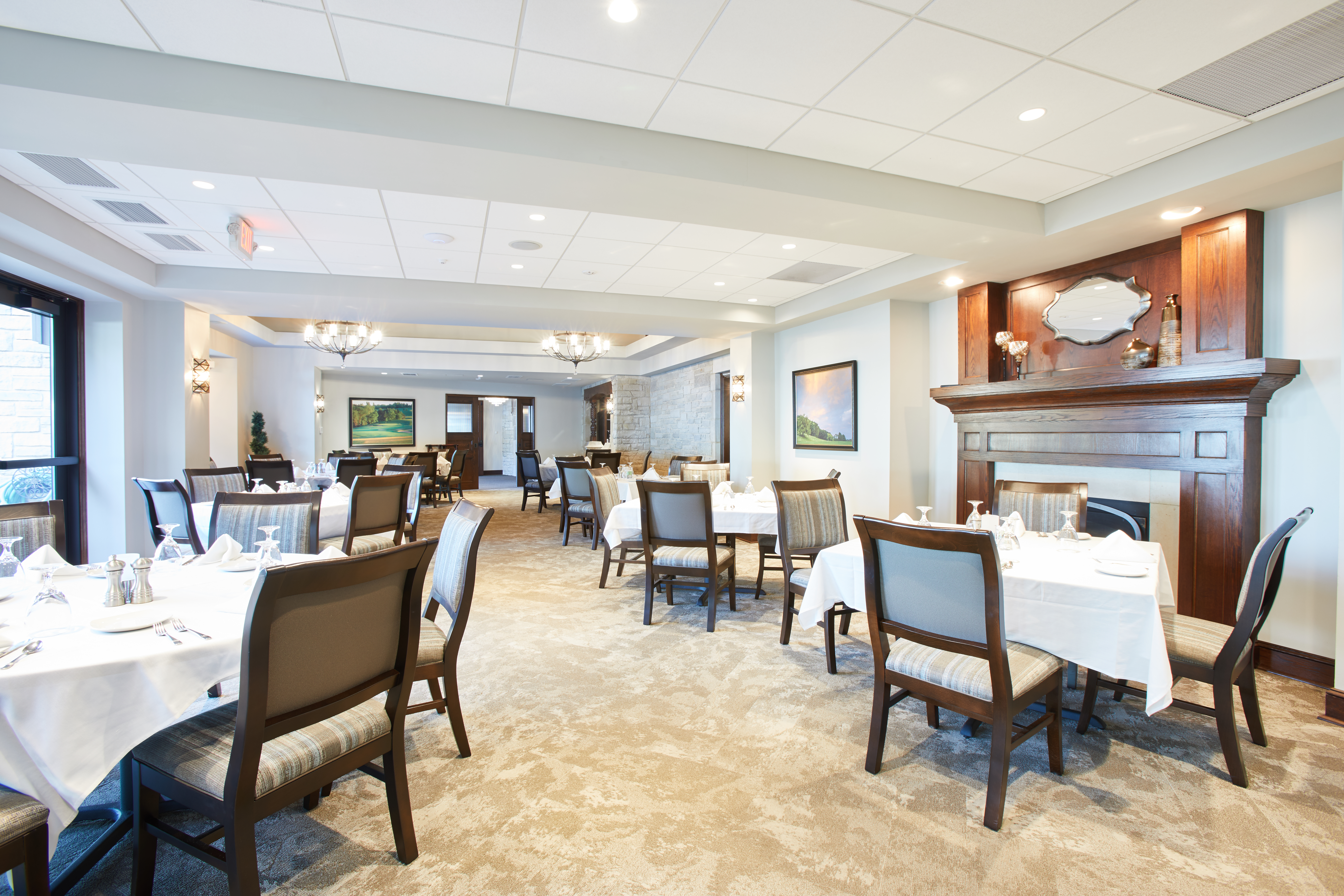 Bishops Bay Country Club restaurant seating with white tablecloths, white walls, and wood panel fireplace