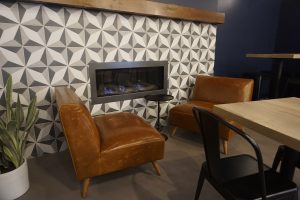 Espresso bar fireplace with white and gray tiles, two brown leather lounge chairs frame the fireplace