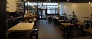 wide view of the entire espresso bar with high black ceilings, string lights, wood table top seating, and large espresso bar