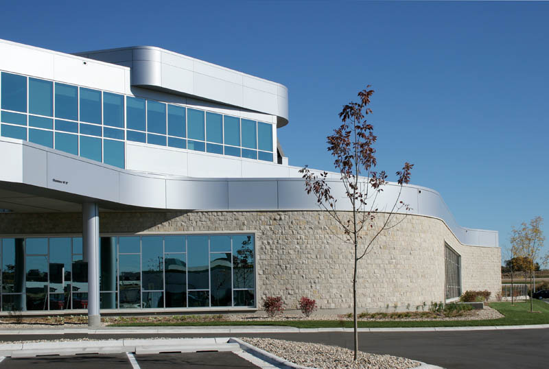 A modern building with large glass windows and curved white metal panels on the upper floors. The ground floor features a stone facade.