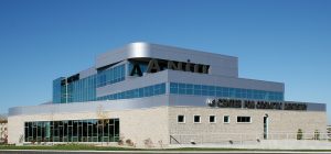 Show thumbnail preview A modern multi-story building with a sleek, glass facade, and a distinctive architectural design. The structure features prominent signage that reads "Center for Cosmetic Dentistry" against a clear blue sky, with neatly landscaped surroundings and a pathway.