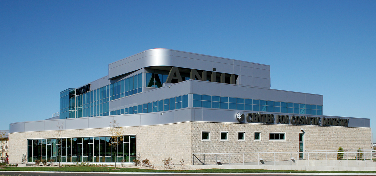 Show thumbnail preview A modern multi-story building with a sleek, glass facade, and a distinctive architectural design. The structure features prominent signage that reads "Center for Cosmetic Dentistry" against a clear blue sky, with neatly landscaped surroundings and a pathway.