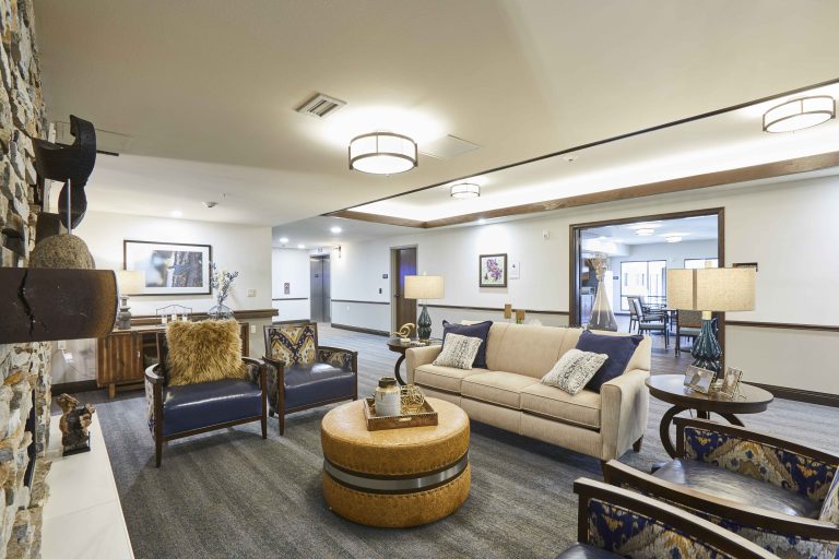 Senior Living facility common seating area with a tan couch, dark gray carpet and modern lighting