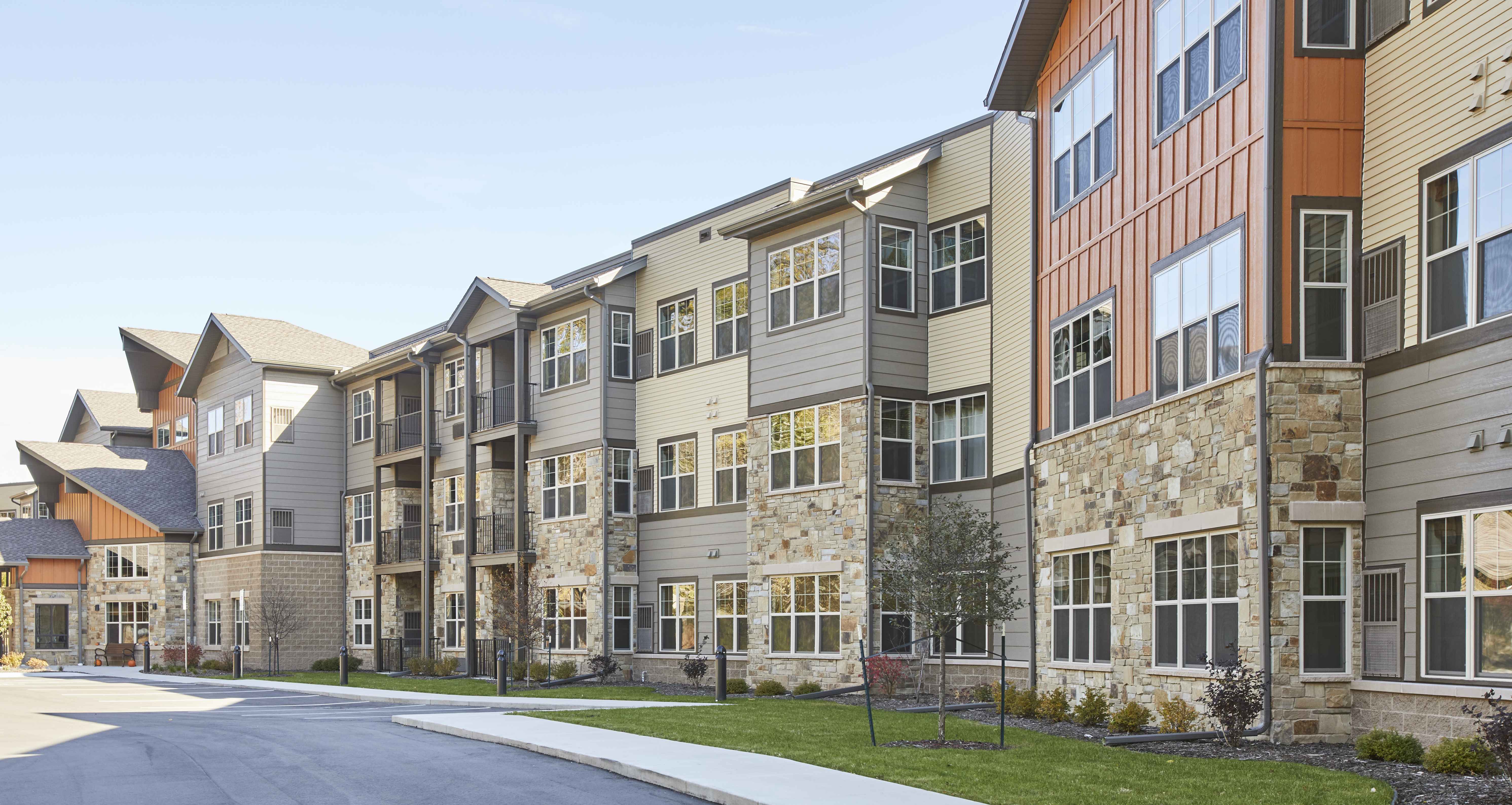 3 story senior living facility exterior with mixed siding of stone, vinyl cream, gray and orange tones