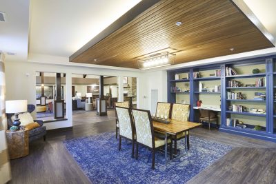 Senior Living facility library with wood floors, a blue carpet centering the room with blue book shelves a table and chairs