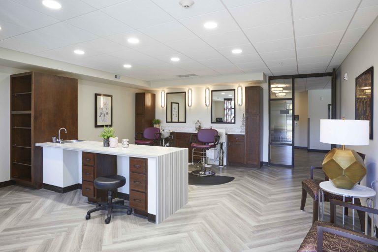 A senior living facility salon with gray herringbone floors a table, mirrors and salon chairs