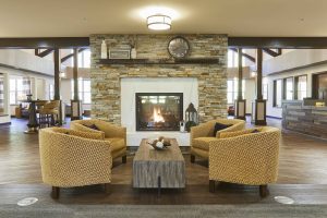 senior living lounge area with oversized cream chairs in front of a stone fireplace