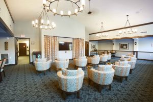 A senior living facility theater room with cream colored lounge chairs, cream walls and modern chandeliers