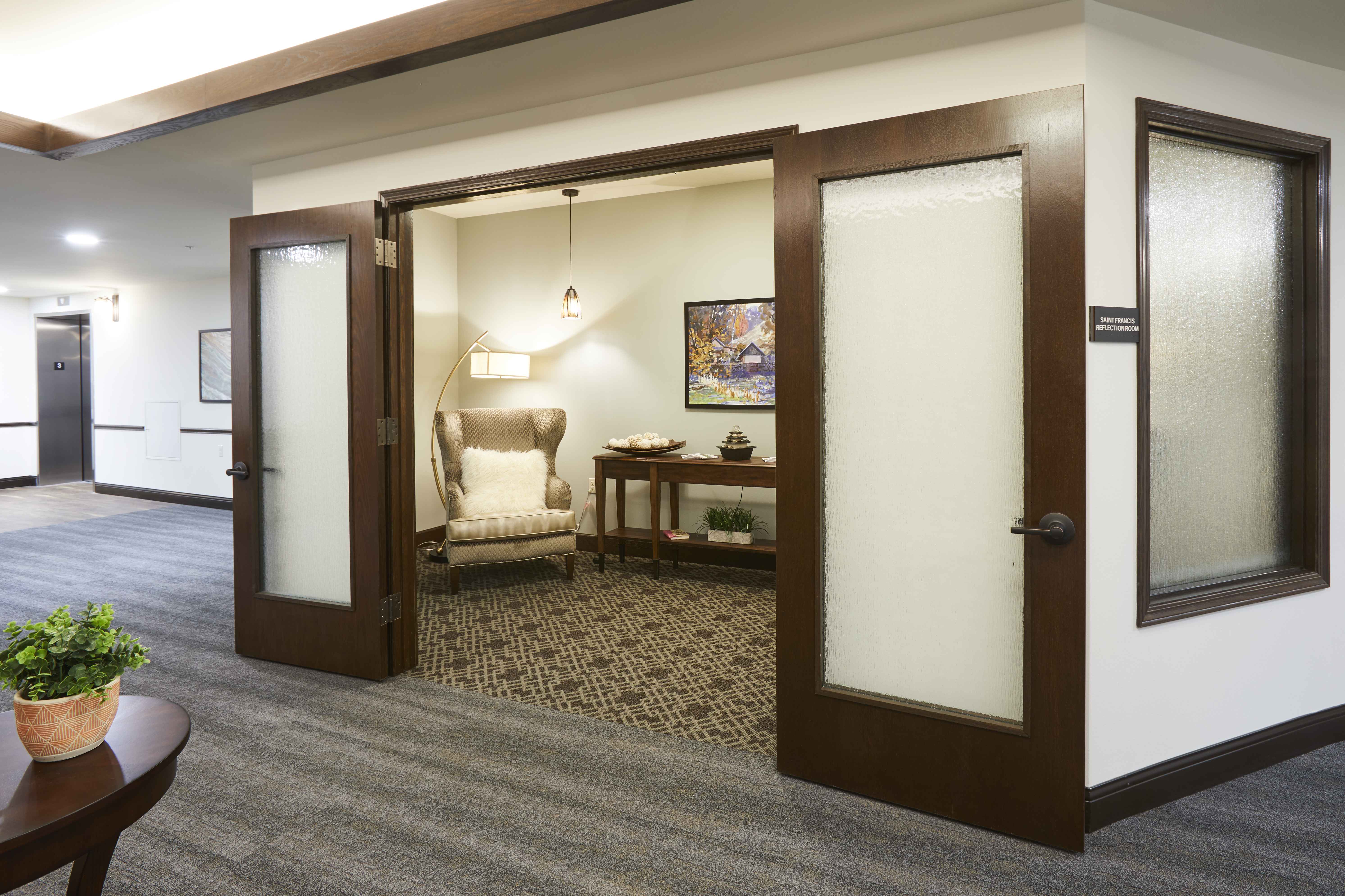 A senior living facility private reflection room with the doors open that show a small calm room with comfortable seating