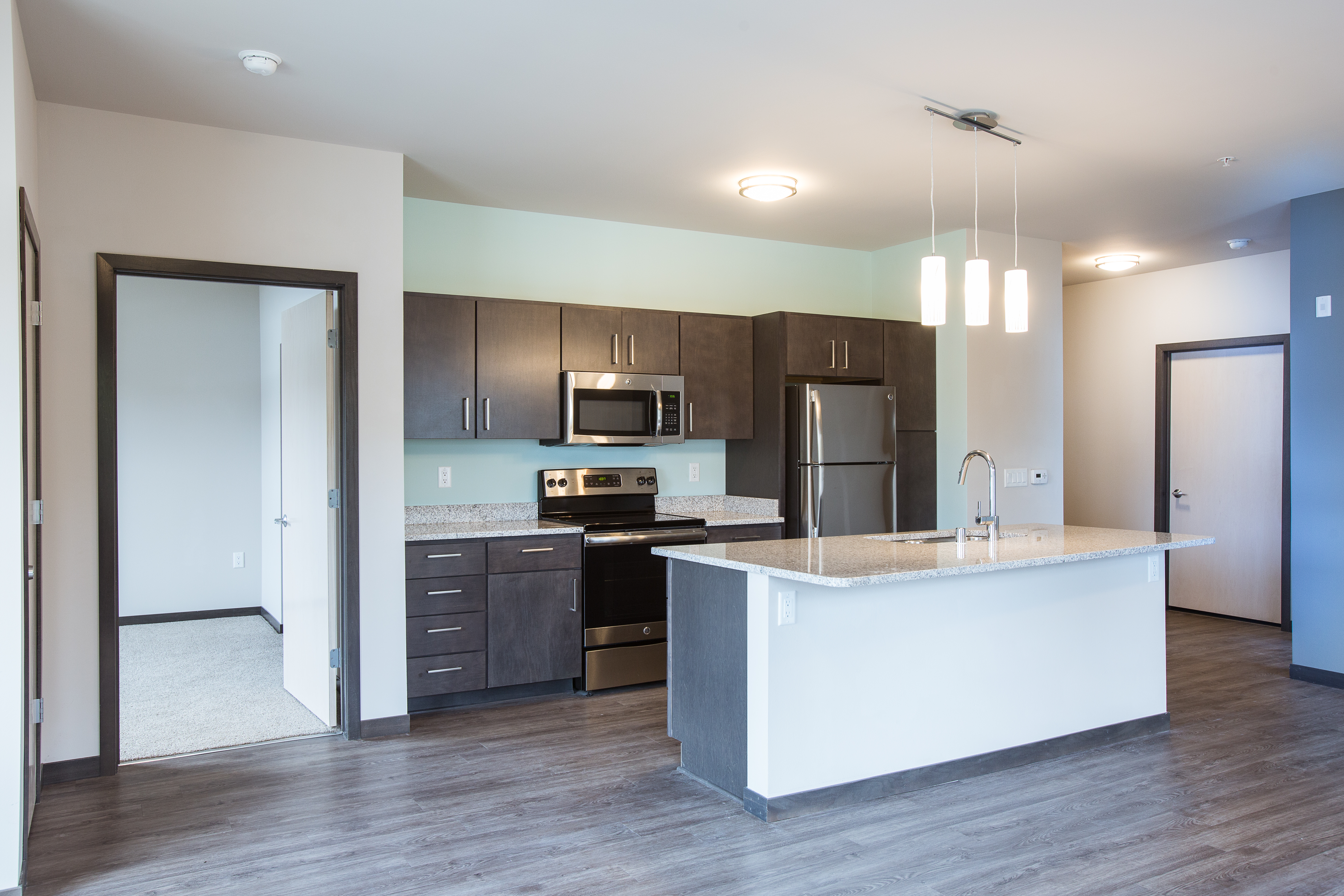 Side view of kitchen with dark cabinets and a white island with granite countertops and hanging lights above the island