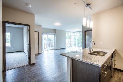 view from kitchen looking into the dining and living space that features a glass patio door and floor to ceiling windows spanning from corner to corner