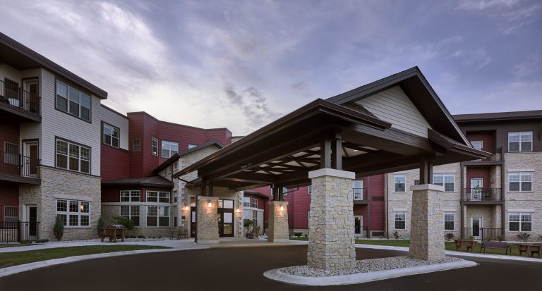 Exterior covered drive up entrance to senior living facility with cream colored bricks and red accent siding