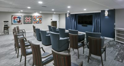 Theater with light gray walls, can lighting and quilt patterned wall art, a tv is mounted on the wall with a dark blue accent wall