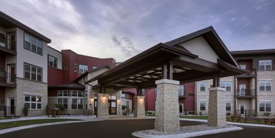 Exterior covered drive up entrance to senior living facility with cream colored bricks and red accent siding