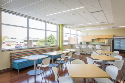 office dining area with wood top tables, naturally lit with large windows and natural wood flooring