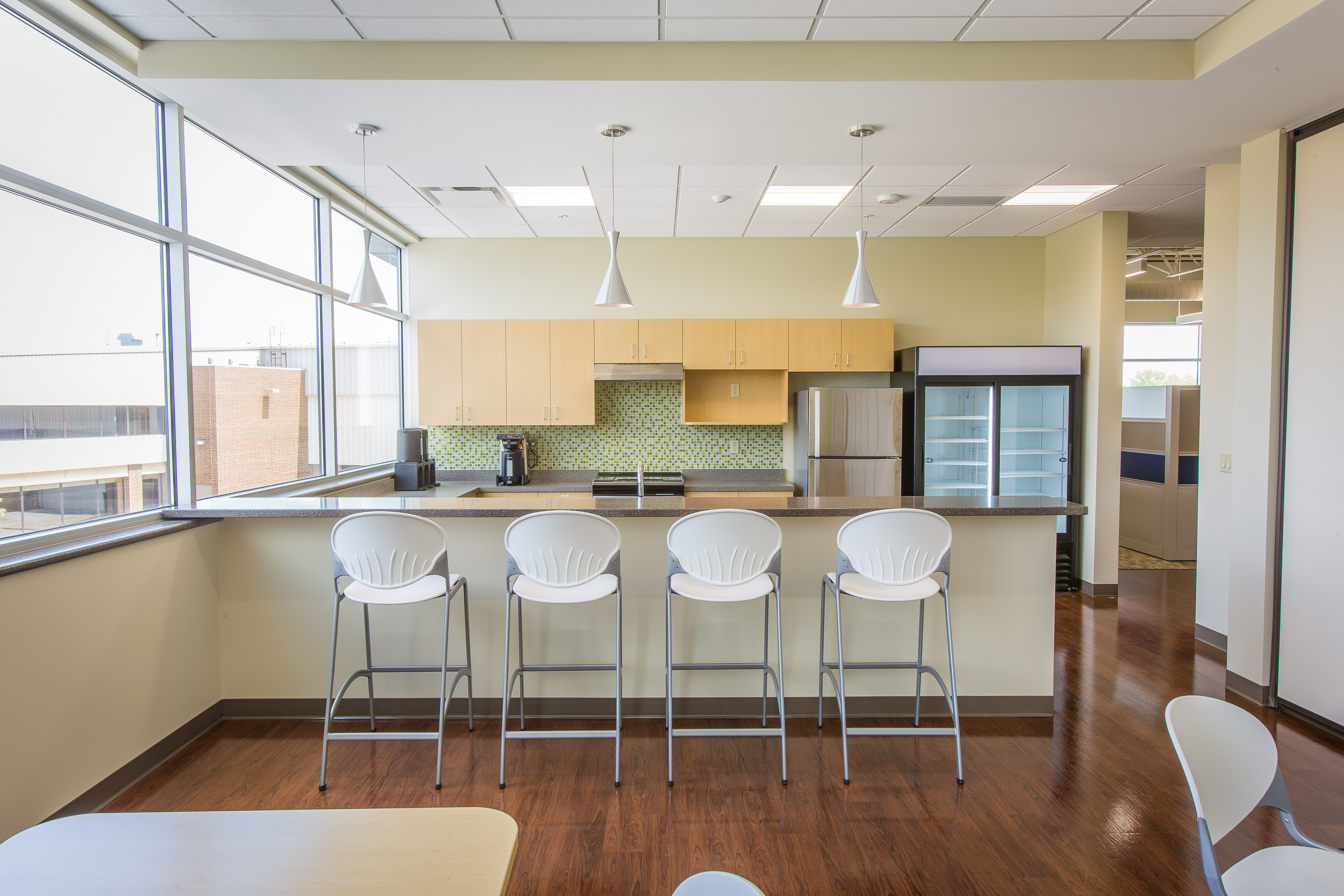 Office kitchen space with island, bar height stools and hanging lights