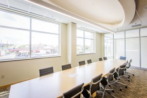 office conference room with natural lighting light colored walls, large wood top rectangular table and black chairs