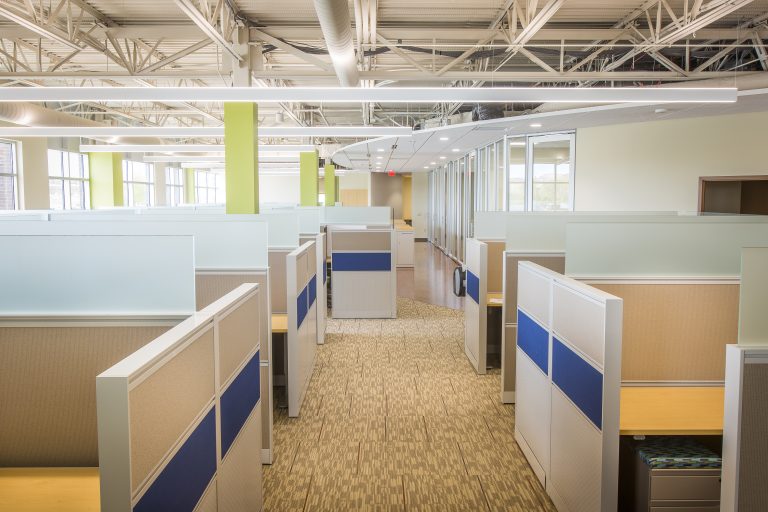 exposed ceiling office space with cubicles neon green accent pole and light color carpeted flooring