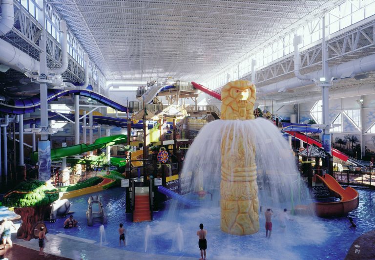 Indoor waterpark with multi-colored slides, shallow pool and water tower spraying out water