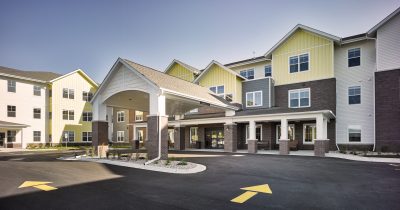 Exterior of Senior living with drive up entrance dark colored bright with white and yellow siding