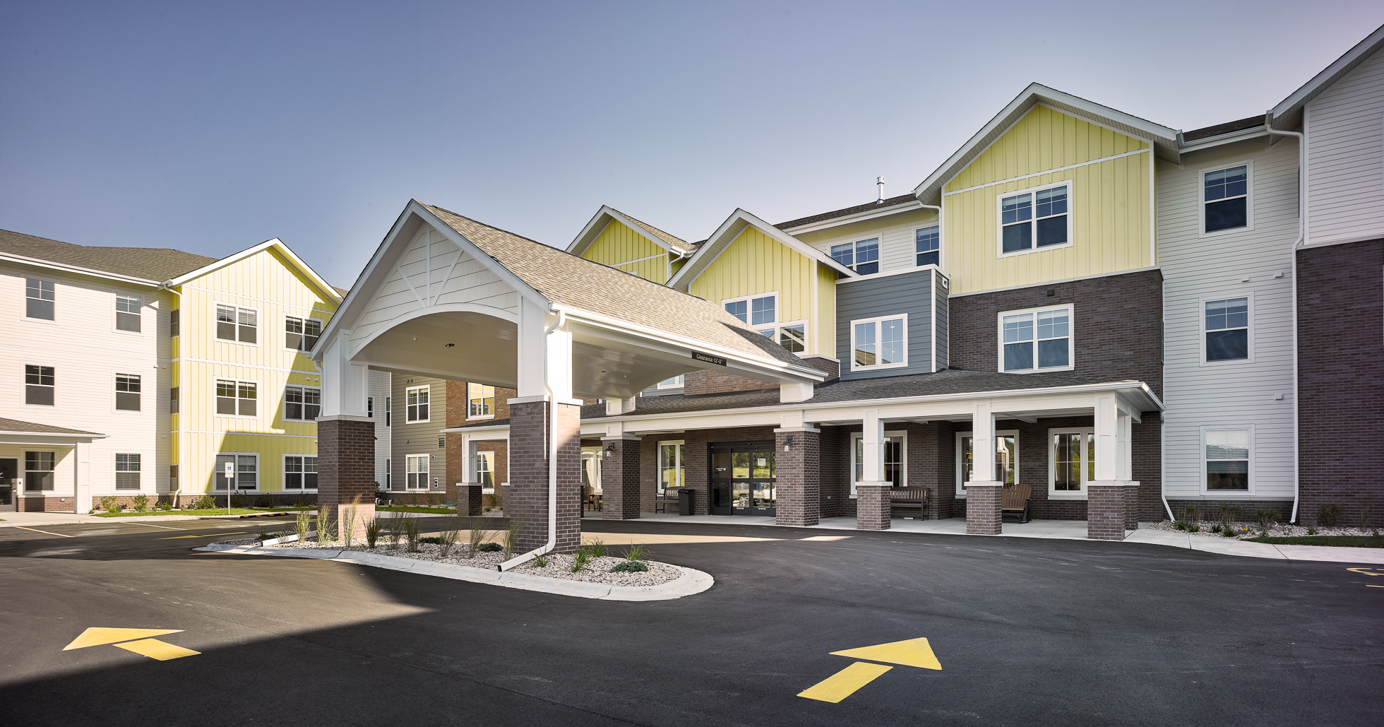 Exterior of Senior living with drive up entrance dark colored bright with white and yellow siding