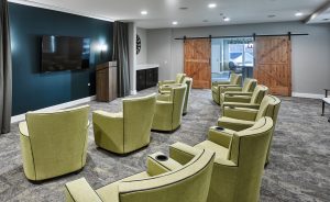 Theater room with gray carpeting, light green reclining chairs with teal colored accent wall and monitor tv mounted on the wall