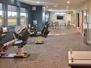 senior living fitness room with exercise equipment, gray carpeting and teal colored walls