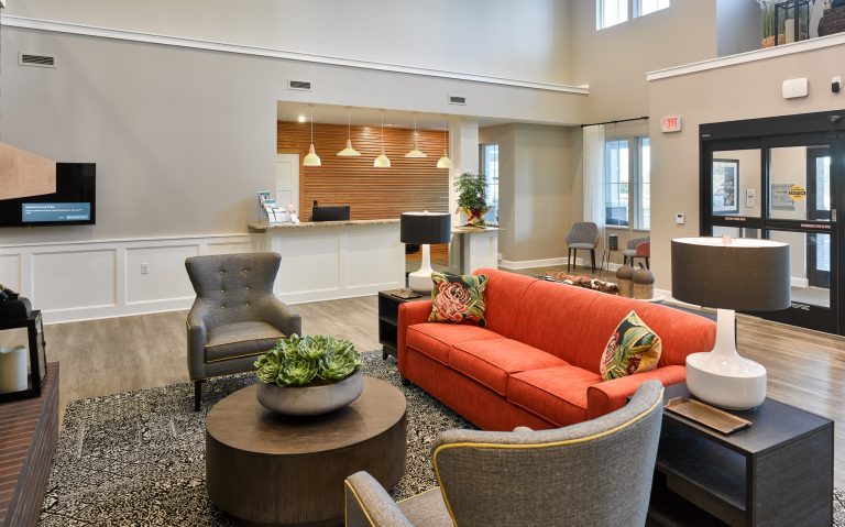 lobby with vaulted ceilings an orange couch and two gray arm chairs