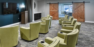 Theater room with gray carpeting, light green reclining chairs with teal colored accent wall and monitor tv mounted on the wall