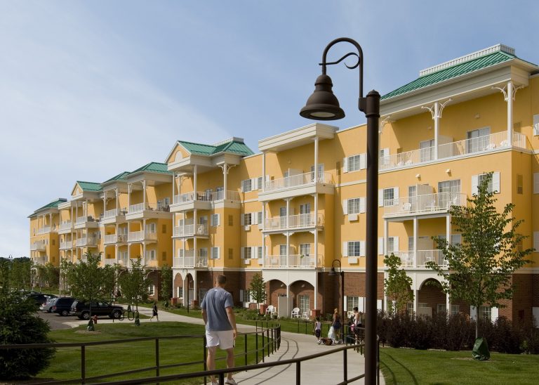 Yellow exterior of hotel of the water resort with white railings and green colored roof