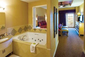 Hotel room with spa tub, light yellow walls and look thru window in the bedroom