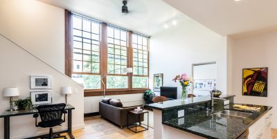 Open concept living room and kitchen with expansive windows, wood flooring and dark colored granite countertops