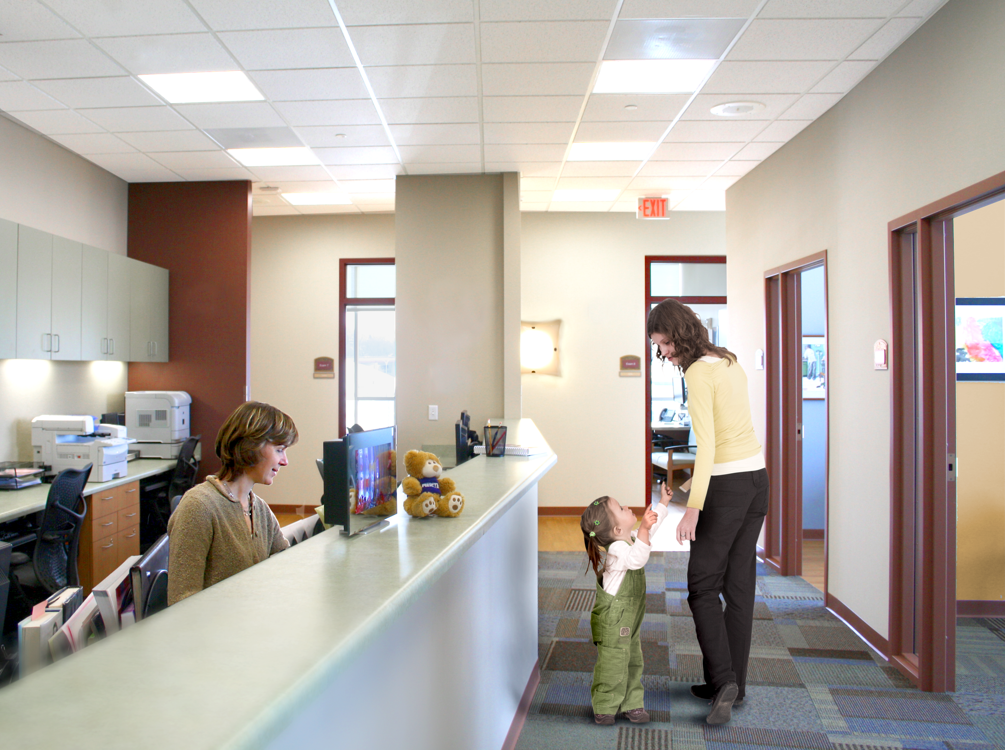 A doctor's office check in area with a mother and young toddler checking in, in the well lit reception area