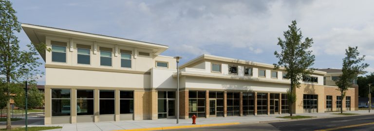 A modern multi-tenant retail building with large windows and a flat roof, surrounded by trees.