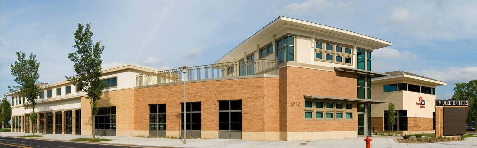 A modern two-story building with a mix of beige, large windows, and a decorative metal awning.