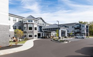 Exterior of senior living facility. It features large windows, a covered entrance, and a paved driveway with parking spaces