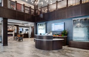 A spacious, modern lobby. The area features comfortable seating, a fireplace, and a TV displaying information. Dark wood accents and contemporary lighting complete the elegant design.