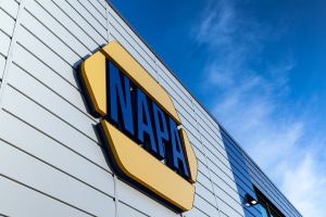 A building with a large, yellow NAPA sign displayed on the side against a blue sky. The structure has white paneling with reflections of the sky on its windows.